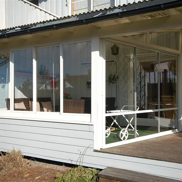 Utestue med hvite rammer og store glassvinduer, med rottingmøbler inne.