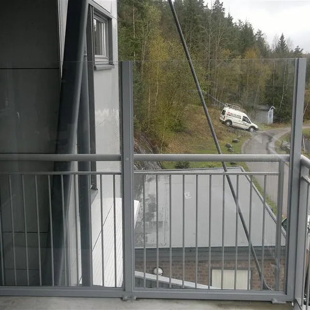 Balkong med kombinasjon av metallrekkverk og klart glasspanel.